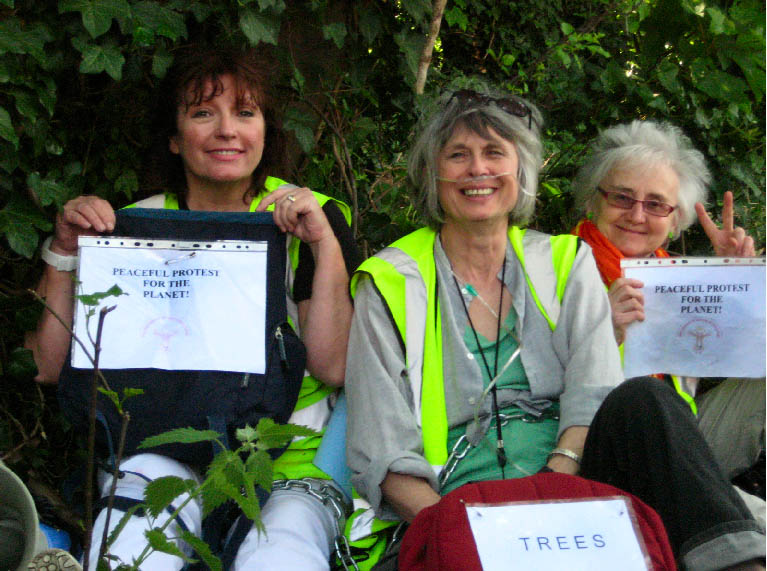 3 women chained to a tree smiling and waving to fellow protesters