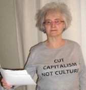 Frankie in a t-shirt saying 'Cut capitalism not culture' reading from a paper.